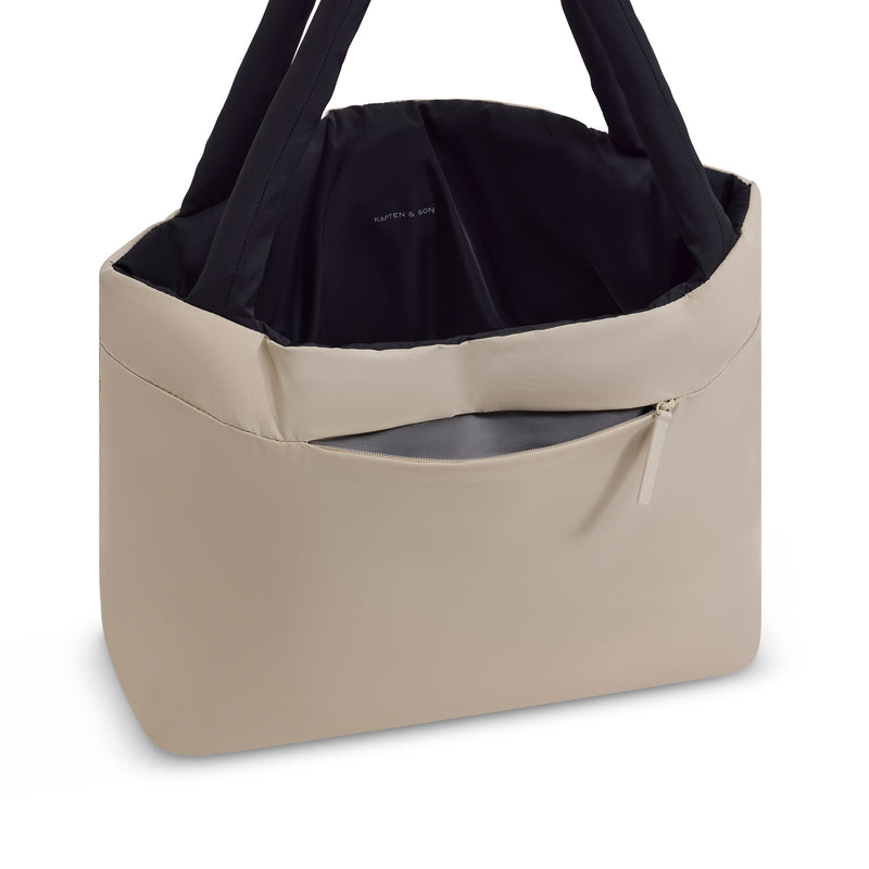 Shopper opened at an angle, sand outside and black lining inside, exterior zip pocket unzipped