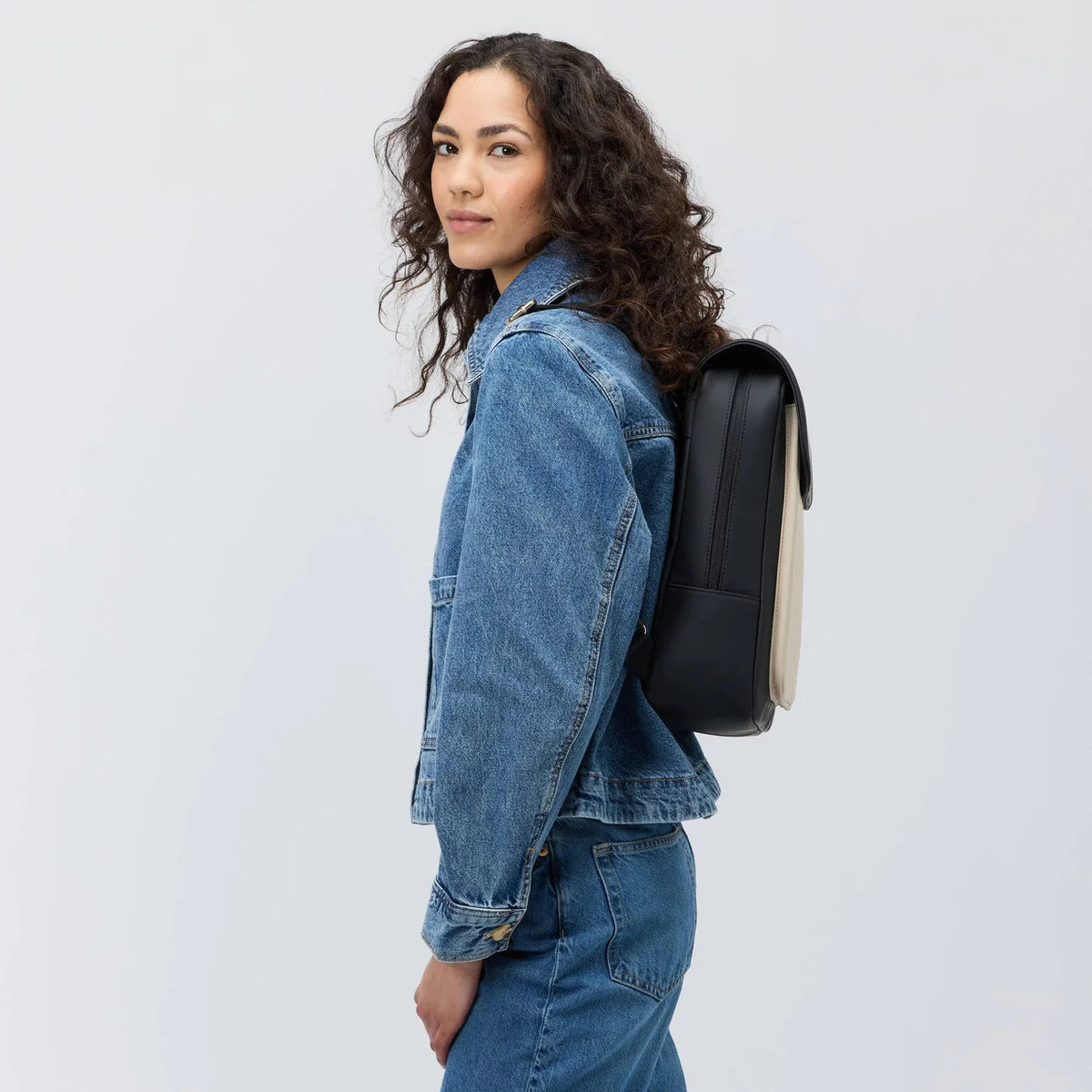 Woman wearing the cream black Tromso backpack with a denim jacket, side view
