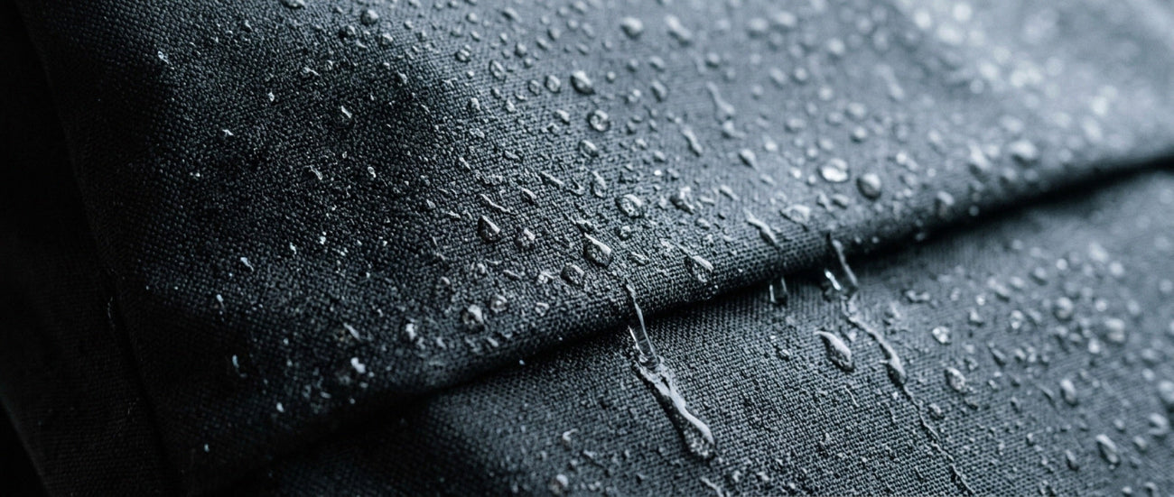Rain beading on the dark coated fabric of a roll-top backpack