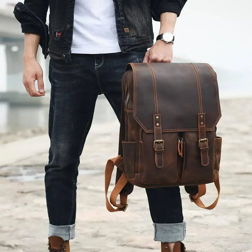 man holding by the top carry handle a vintage full grain crazy horse leather backpack