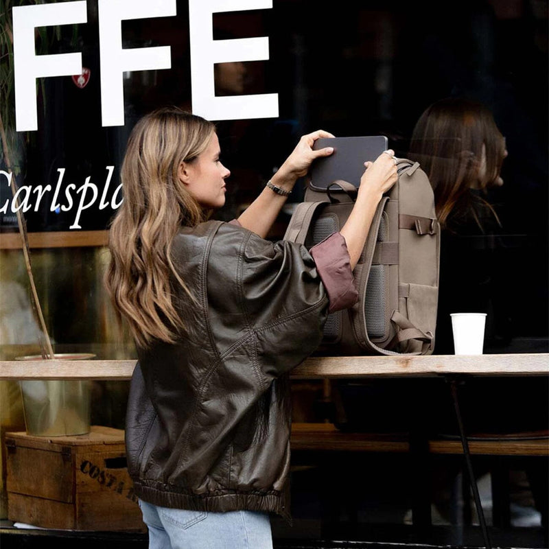 Woman placing her laptop inside the Bali Medium Backpack Walnut by Kapten & Son while enjoying coffee in a city café — a perfect blend of style and function