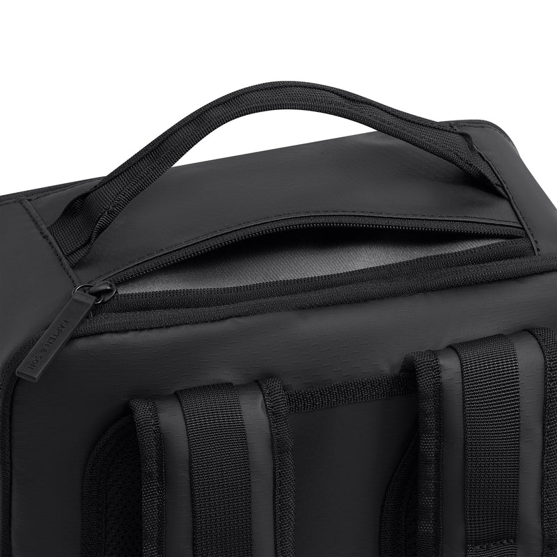Zip of the outer laptop compartment along the top of the back panel of the black Bergen Ultra backpack