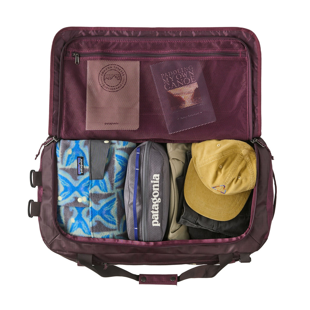 Open Black Hole Duffel 55L in Berry Fig packed with packing cubes, a cap and a notebook