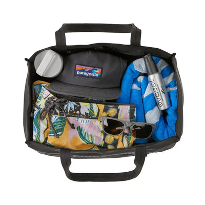Open tote filled with beach essentials: towel, cap, sunglasses and swim shorts