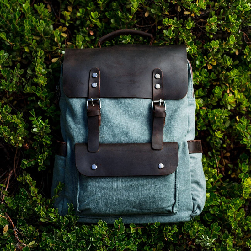 vintage canvas and leather hiking backpack helsinki, dark leather and light blue canvas, laying on forest ground