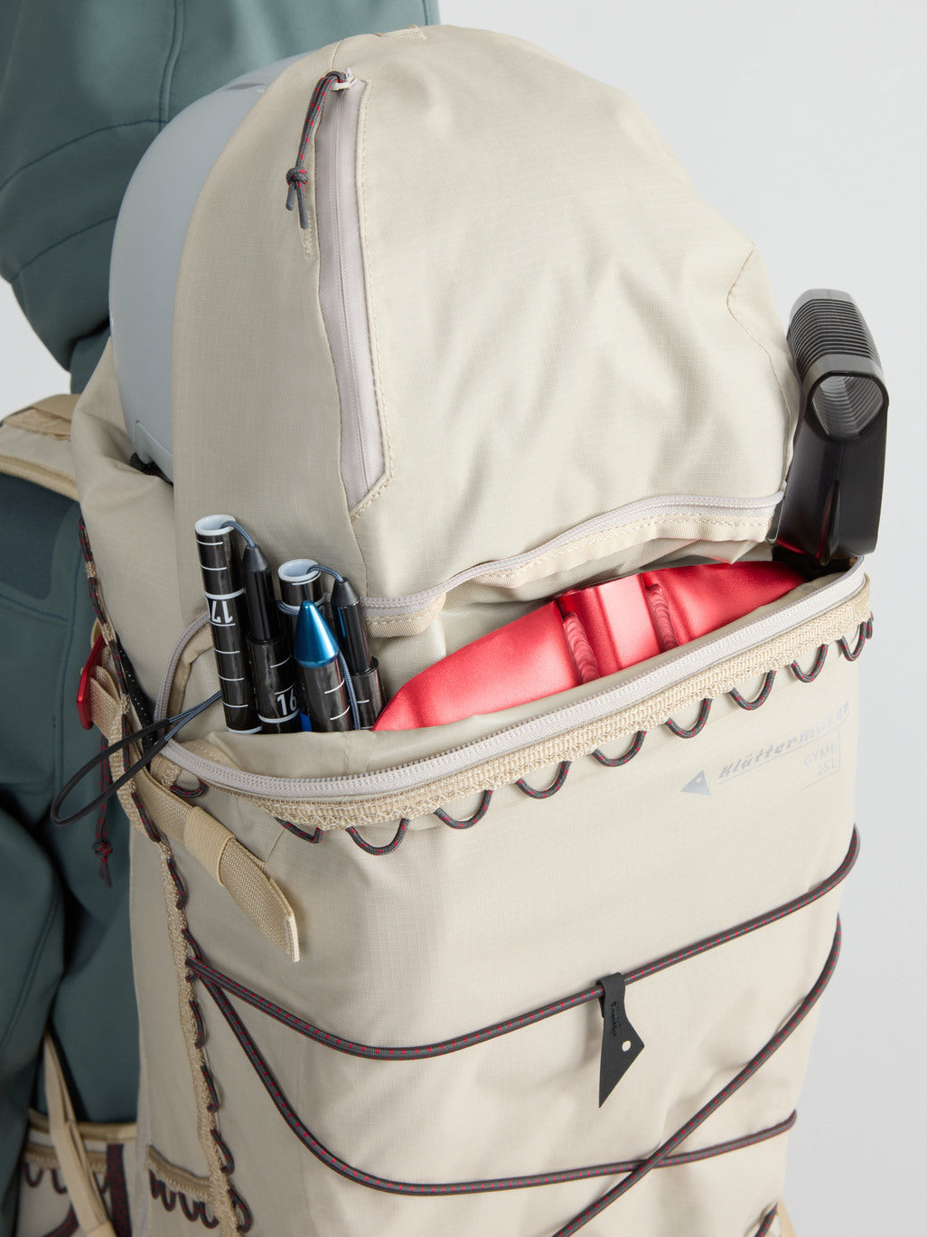 Gyme 25L in Silver Creme with the top compartment open — shovel handle and probe in the red-lined safety pocket