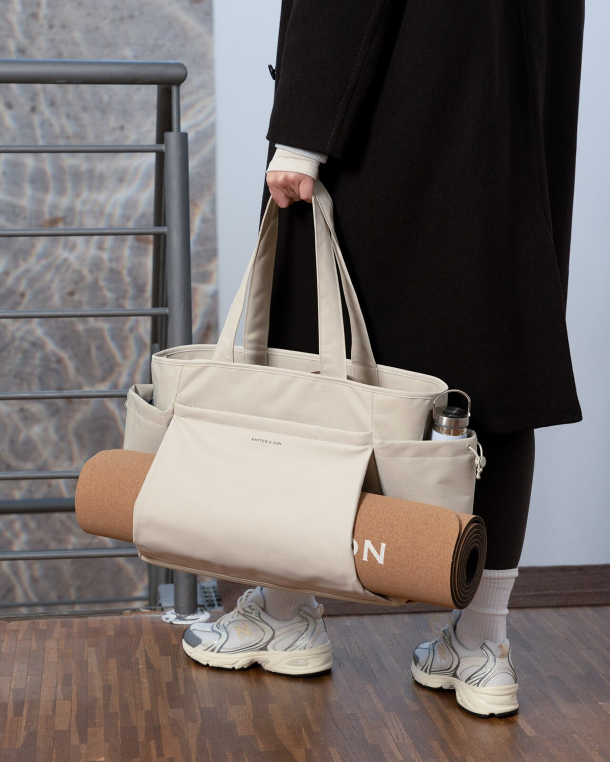 Sandstone Kapten & Son Hellvi Pro Large carried by hand, a cork yoga mat slid across the front