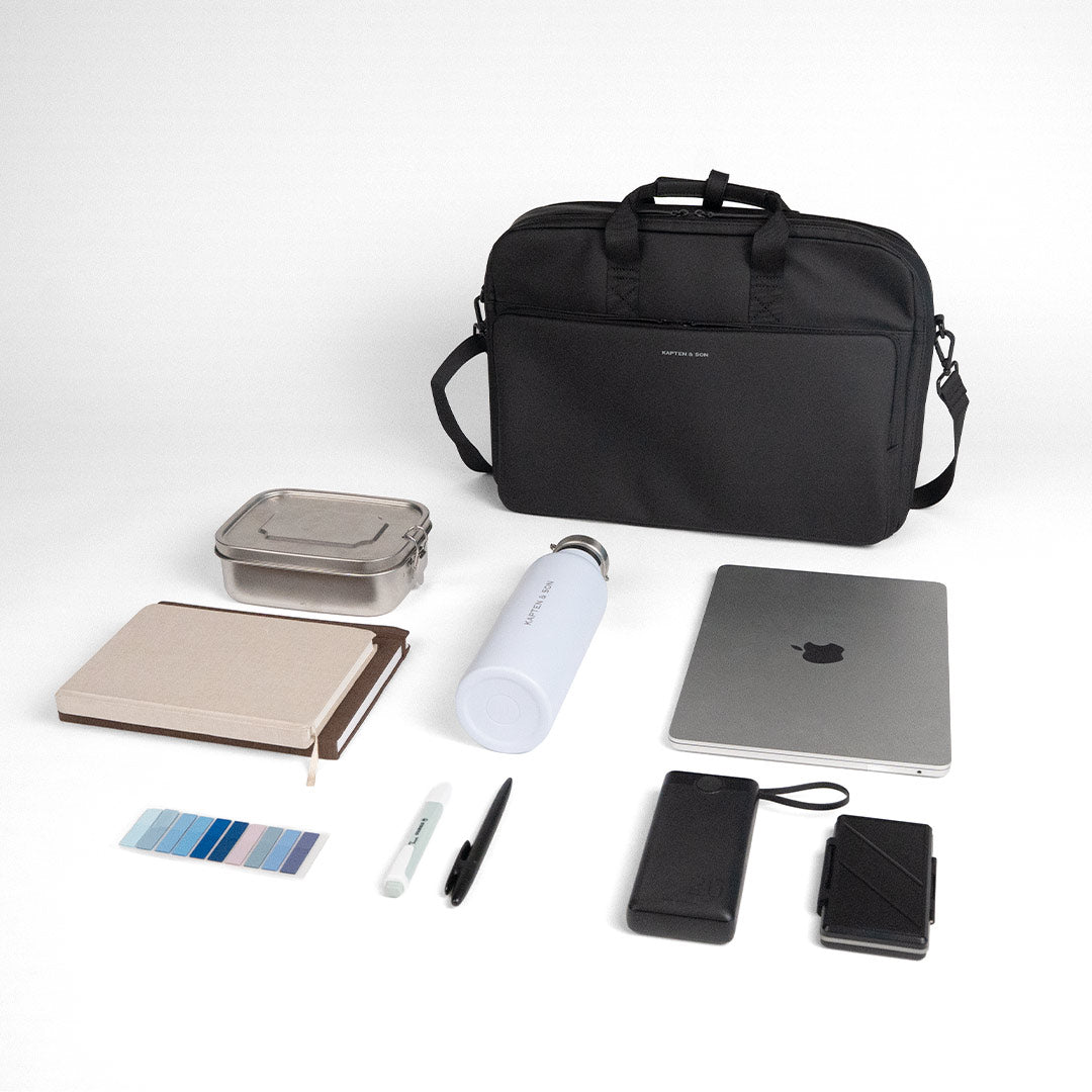 Bodo Laptop Bag in black with a laptop, a lunch box, a notebook, a water bottle, a power bank and pens laid out beside it