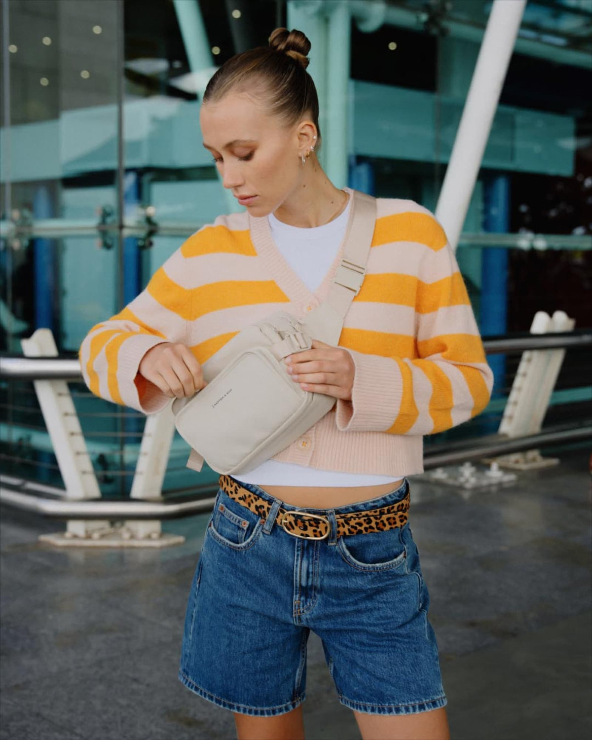 Woman at the airport opening the sandstone Lisbon Crossbody worn on her front