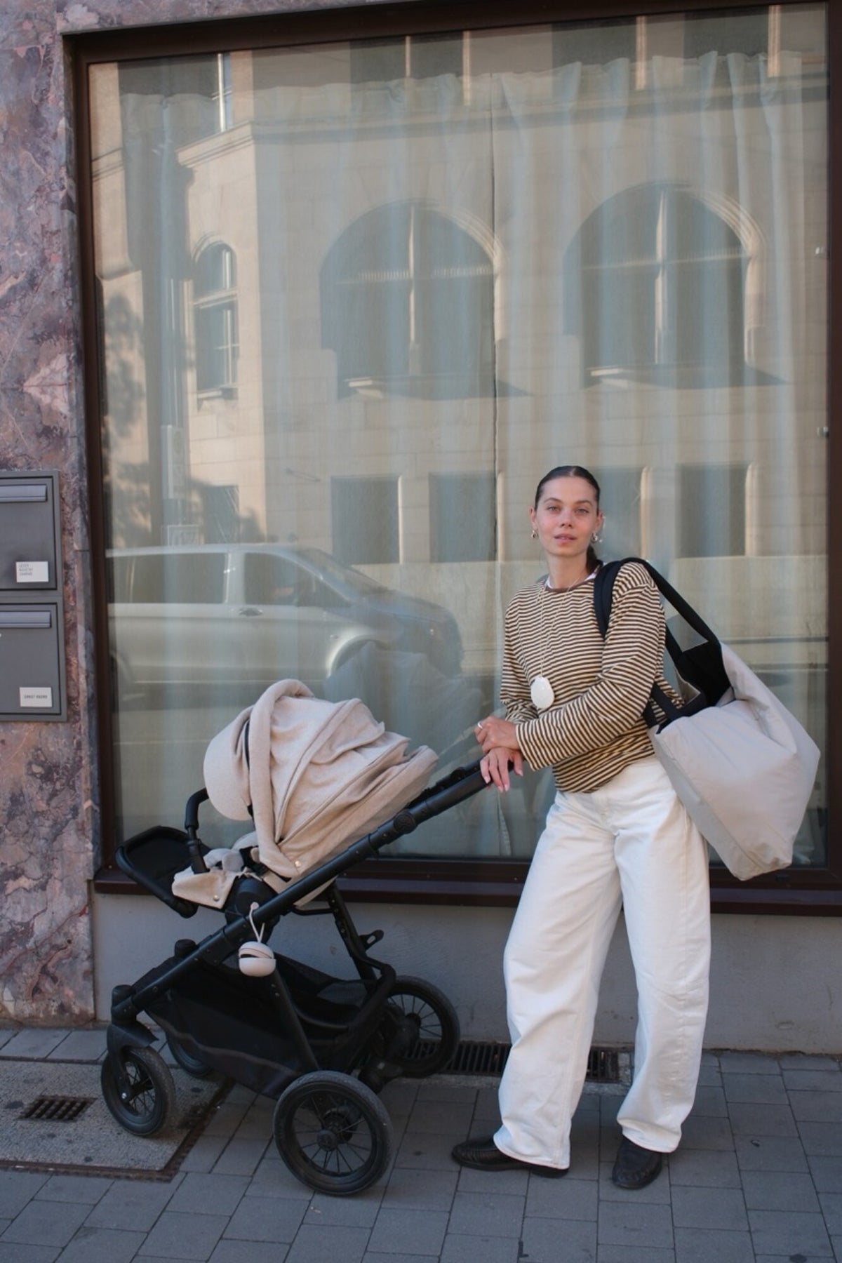 Woman with a pram in the street, the Norva 2in1 Shopper on her shoulder, sand side out