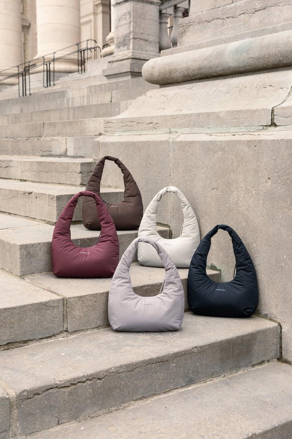 Five Skara Cloud Shoulder bags in different colours on stone steps
