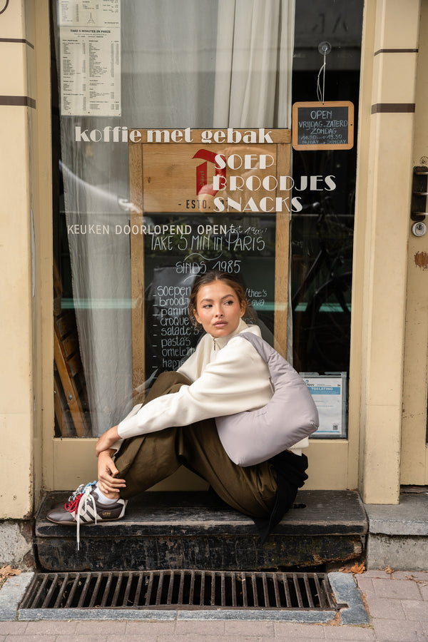 Woman sitting on a café doorstep with the Skara Cloud Shoulder in pale grey
