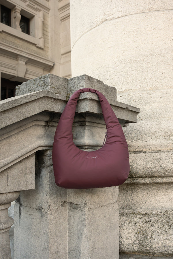 Burgundy Skara Cloud Shoulder resting on a stone ledge