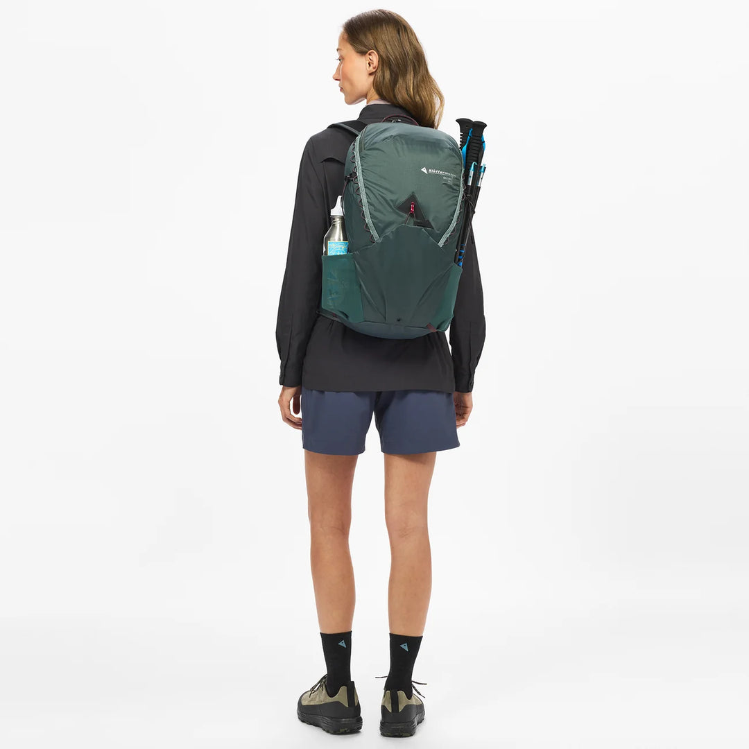 Klättermusen Gilling 20L Dark Teal — worn with trekking poles, back view