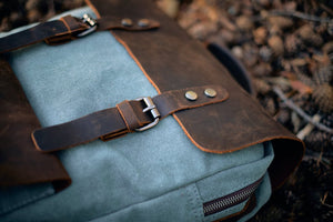 sac à dos vintage bleu clair helsinki en toile de coton et cuir pleine fleur posé sur un sol de forêt de pommes de pin