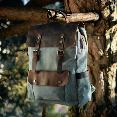 vintage canvas and leather travel backpack in light blue, hanging from a tree branch