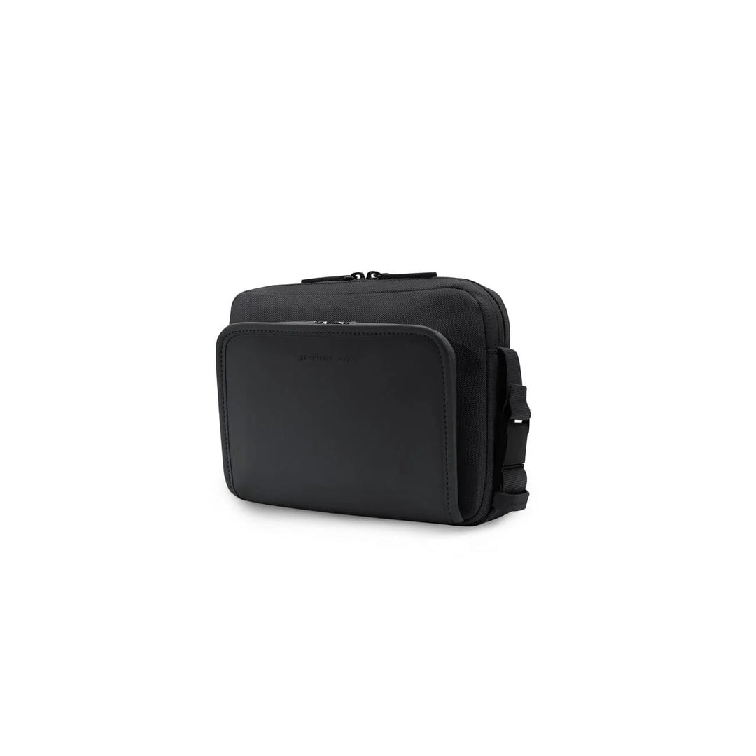 Three-quarter view of the Lulea small crossbody in black showing the smooth leather front panel and canvas body