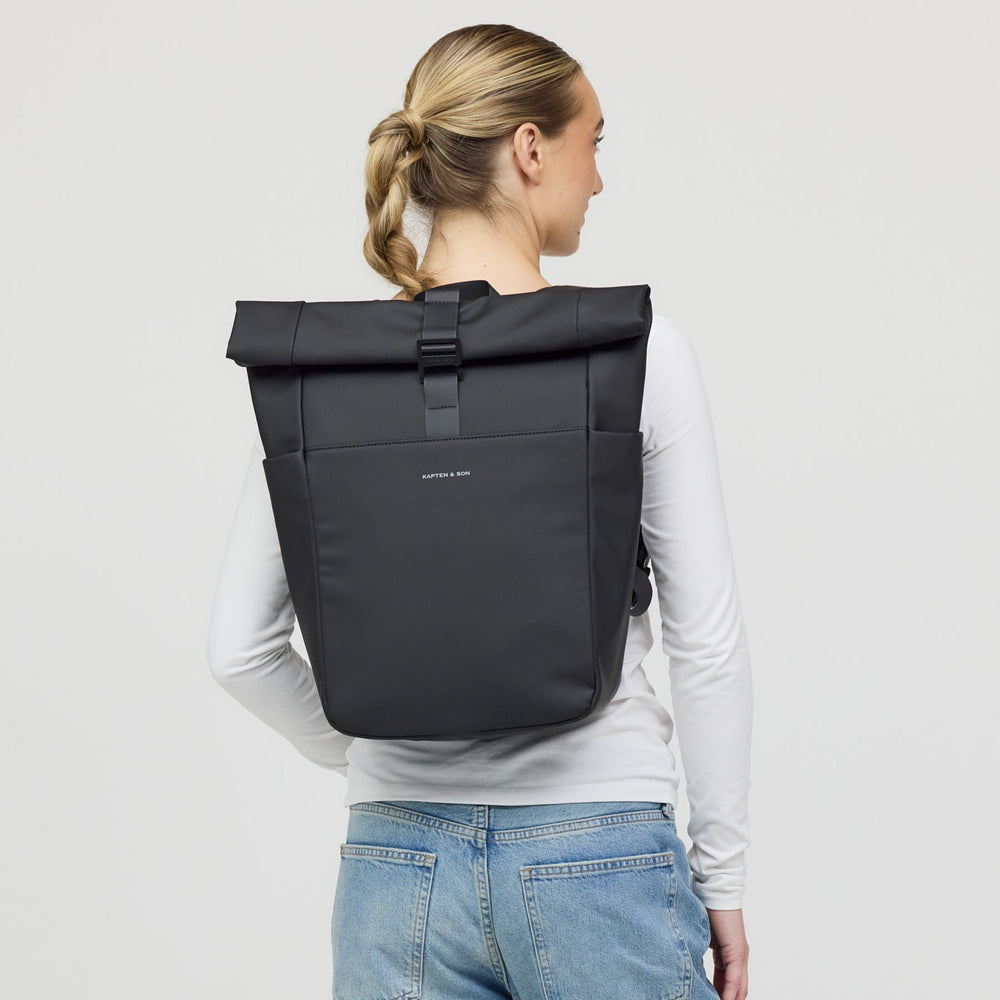 Woman wearing the all black rolltop backpack on her back, casual long-sleeve outfit