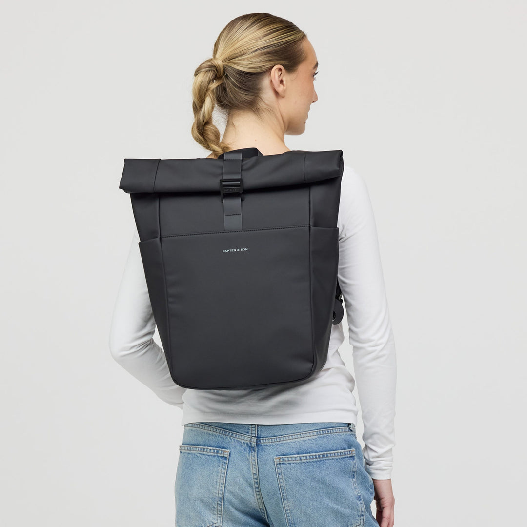 Woman wearing the all black rolltop backpack on her back, casual long-sleeve outfit