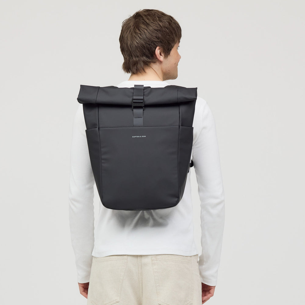 Man wearing the all black rolltop backpack on his back, urban casual outfit