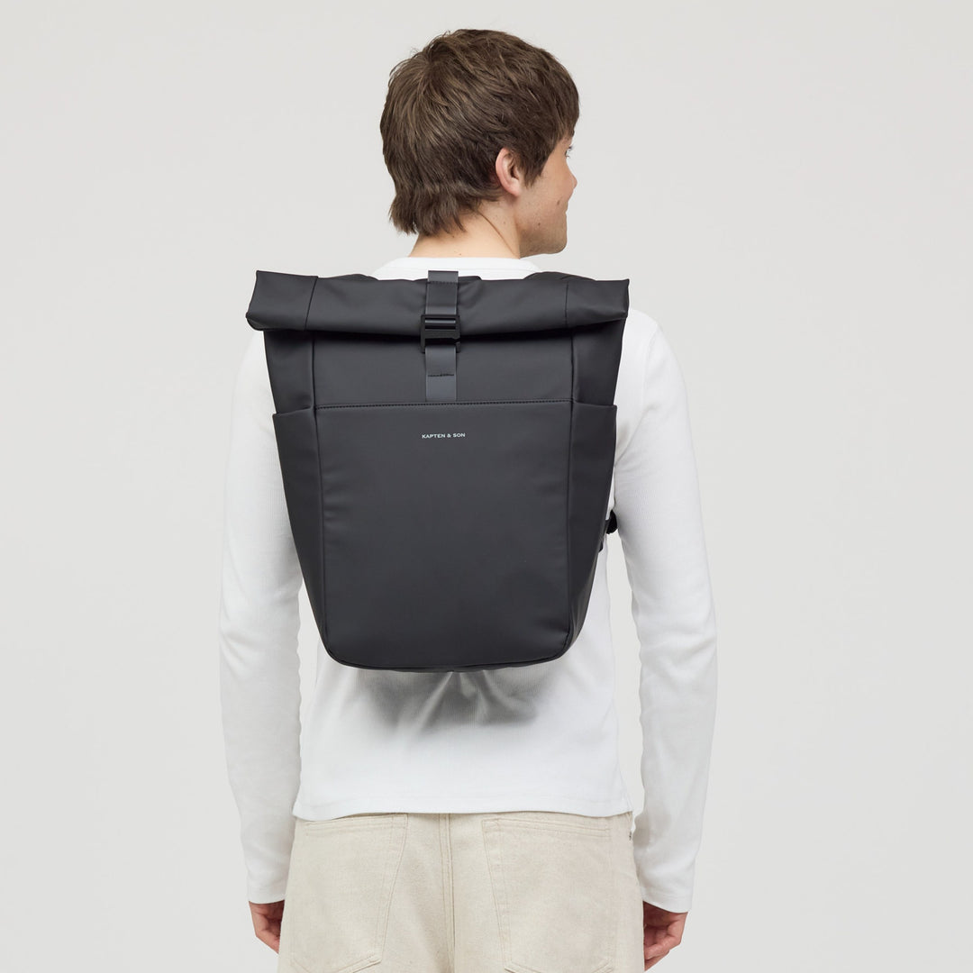 Man wearing the all black rolltop backpack on his back, urban casual outfit
