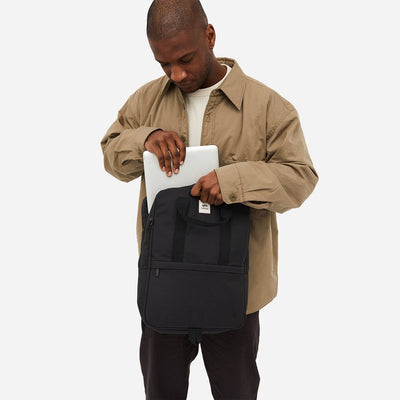 Man from the back storing his laptop in the eco-friendly black backpack on a white background