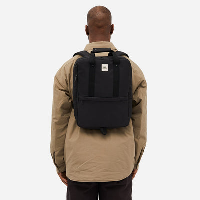 Man seen from the back carrying a sleek black backpack on a white background