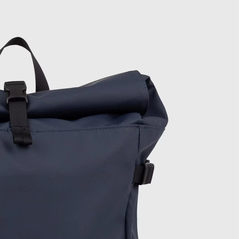 Rolltop closure of the navy blue slim backpack with buckle fastening, offering flexible storage and a minimalist waterproof design