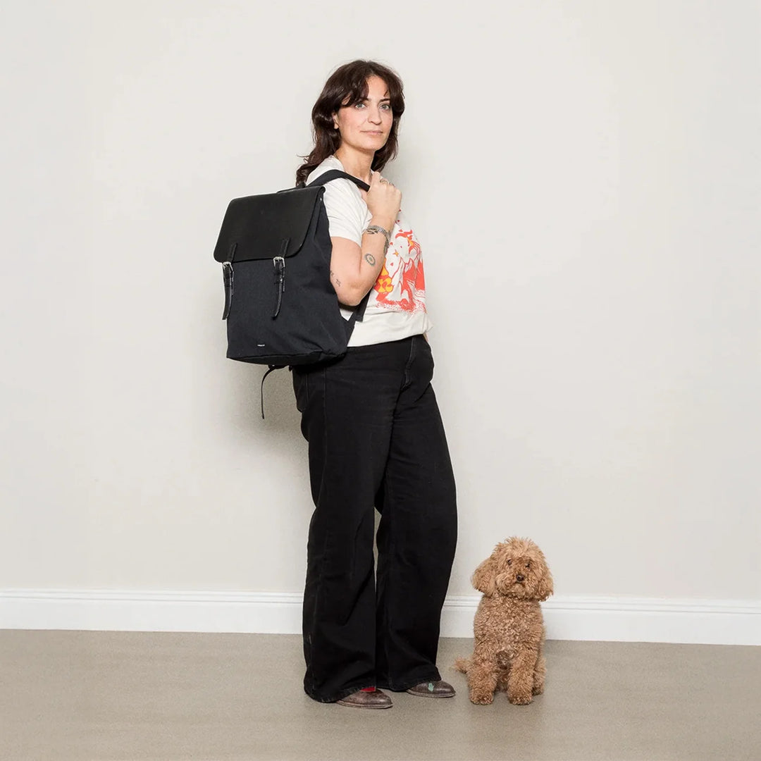 Lifestyle shot — woman wearing the backpack on one shoulder standing next to her dog