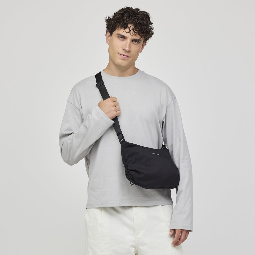 Man wearing the black Skara Small crossbody over a grey sweatshirt, front view