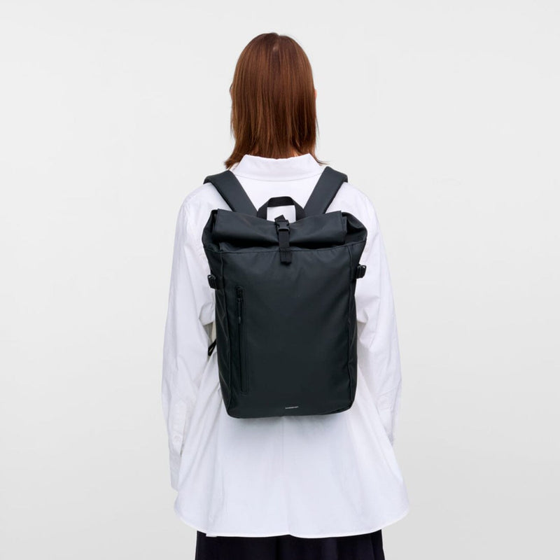 Back view of model wearing the slim black rolltop backpack, showing ergonomic straps and a sleek city-ready silhouette