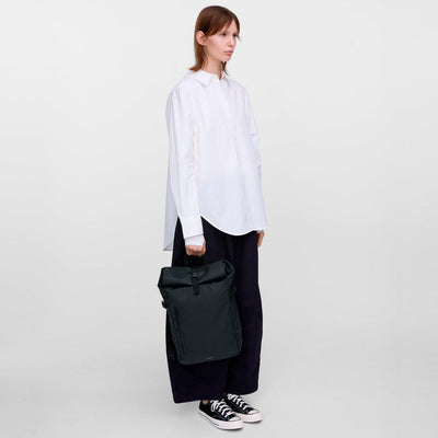 Model carrying the black slim rolltop backpack by hand, showing its minimalist waterproof design and versatile urban style.