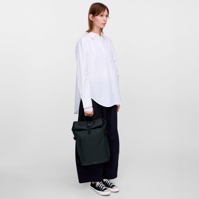 Model carrying the black slim rolltop backpack by hand, showing its minimalist waterproof design and versatile urban style.