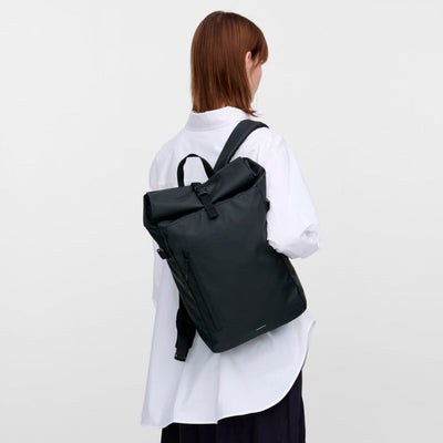 Side profile of model with the Sandqvist slim rolltop M in black, emphasizing its slim shape and comfortable backpack fit