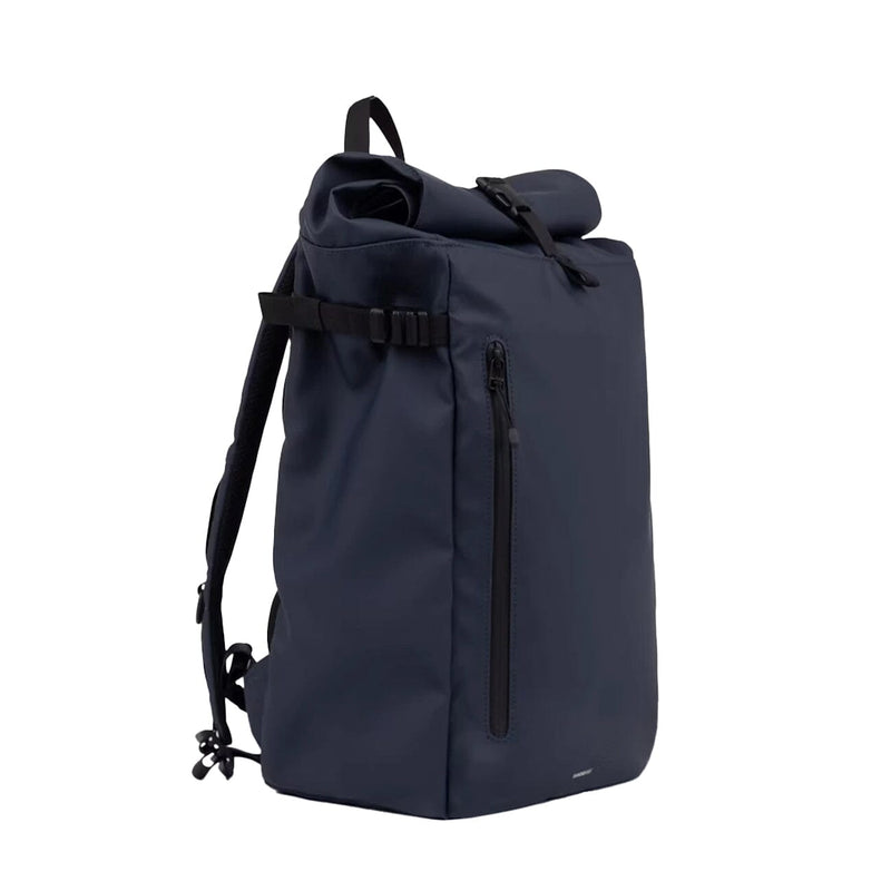 Side angled view of the slim navy rolltop backpack, showing the sleek profile, waterproof zippers, and rolltop closure