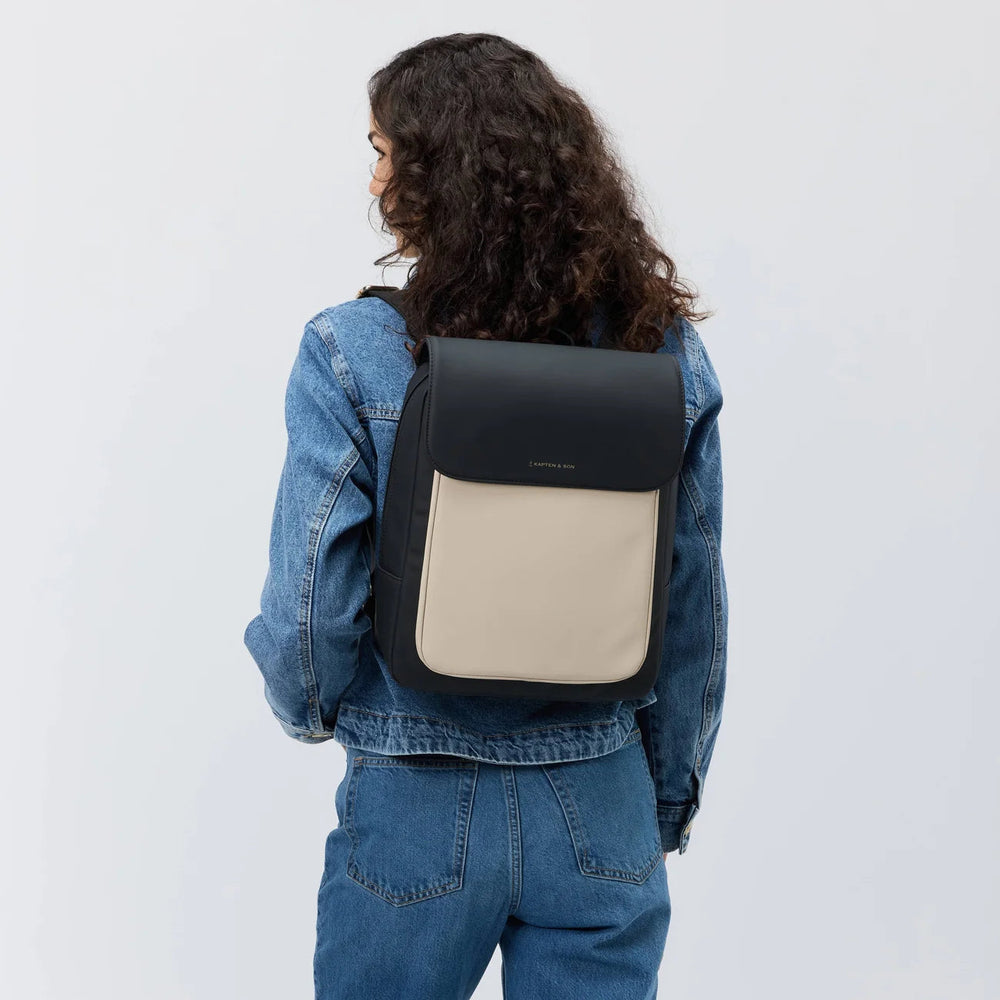 Woman wearing the cream black Tromso backpack with a denim jacket, rear view showing the two-tone design