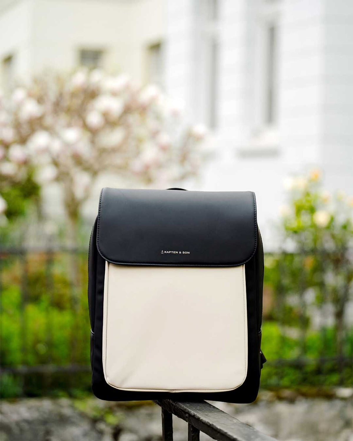 The cream black Kapten & Son Tromso backpack on a wall, magnolias behind