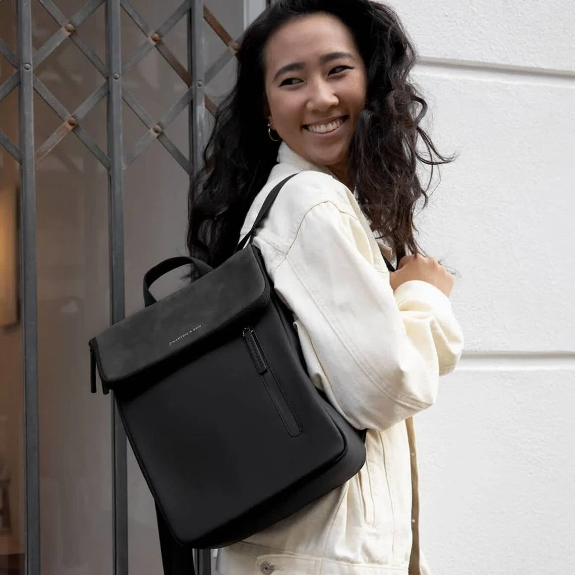 Woman wearing the Kapten & Son Vallen backpack in black with a white jacket in an urban setting