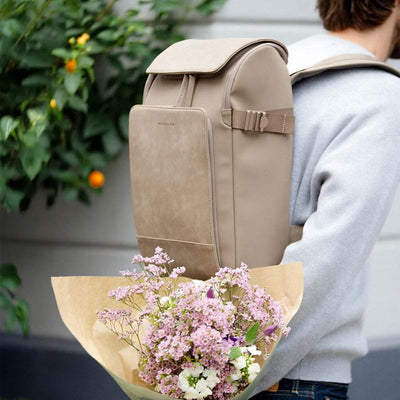 Man carrying the Bali Medium Walnut backpack with a bouquet of flowers, symbolizing a soft yet refined urban style