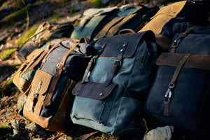 several leather and canvas backpacks from the brand eiken laying on a forest floor