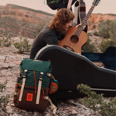 woman camping playing guitar with rover classic pack layed out next to her