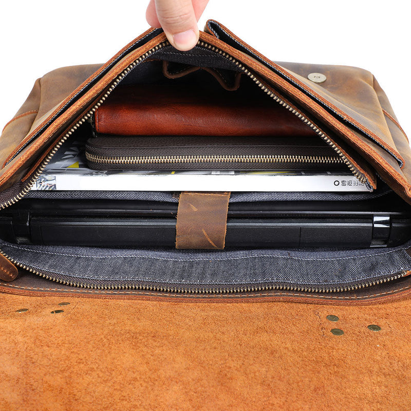 interior of the leather shoulder bag filled with notebooks, magazine, pouches and a laptop