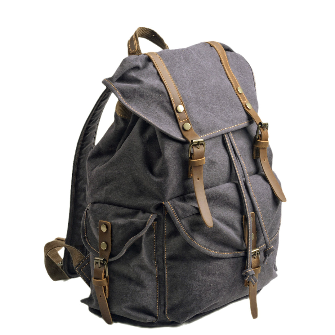 Three-quarter view of the dark grey Montreal canvas rucksack showing depth, side cargo pocket with leather flap and twin strap closures with brass buckles